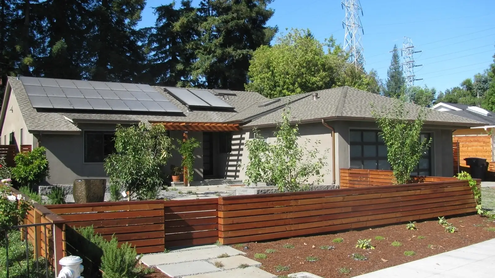 A single-storey house with a rooftop solar array behind a timber fence