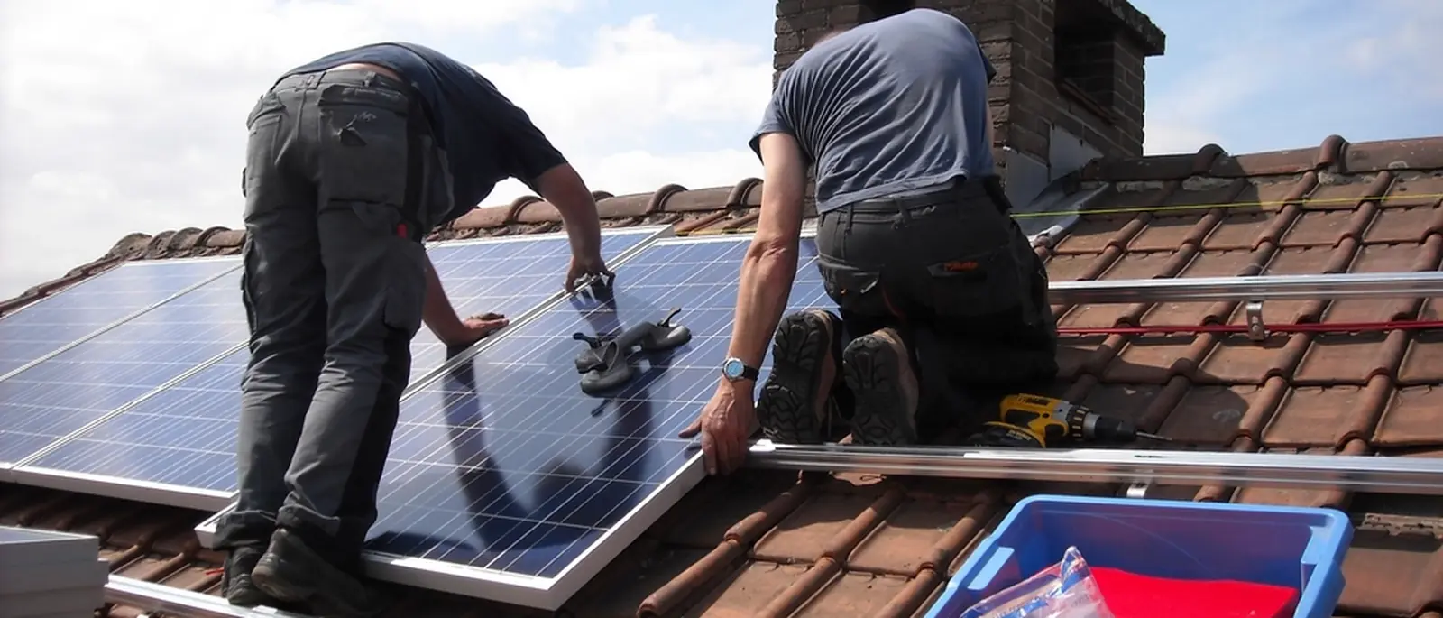 Two installers positioning a solar panel on a tiled roof