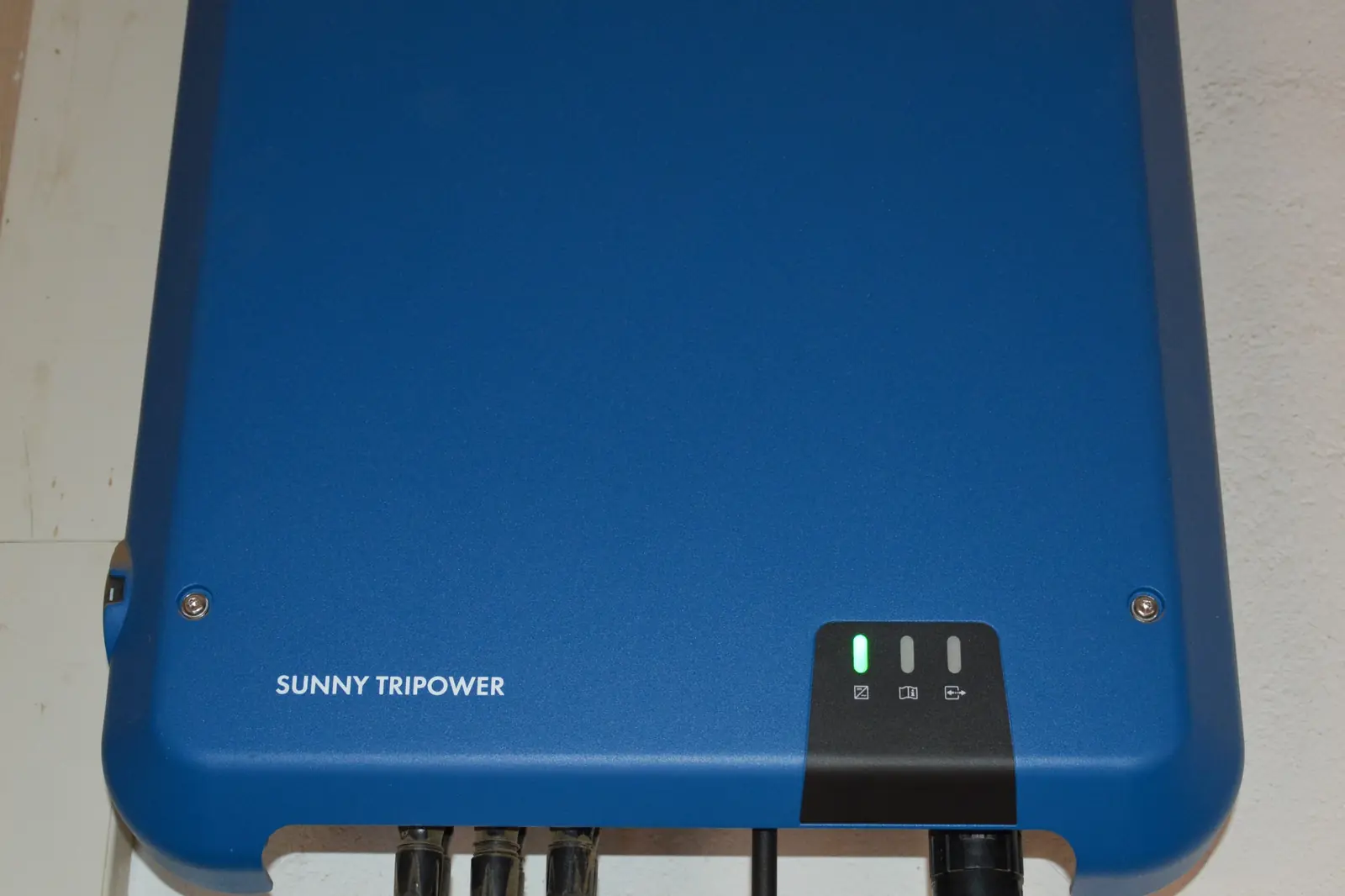 A wall-mounted string solar inverter with DC and AC cabling entering the base