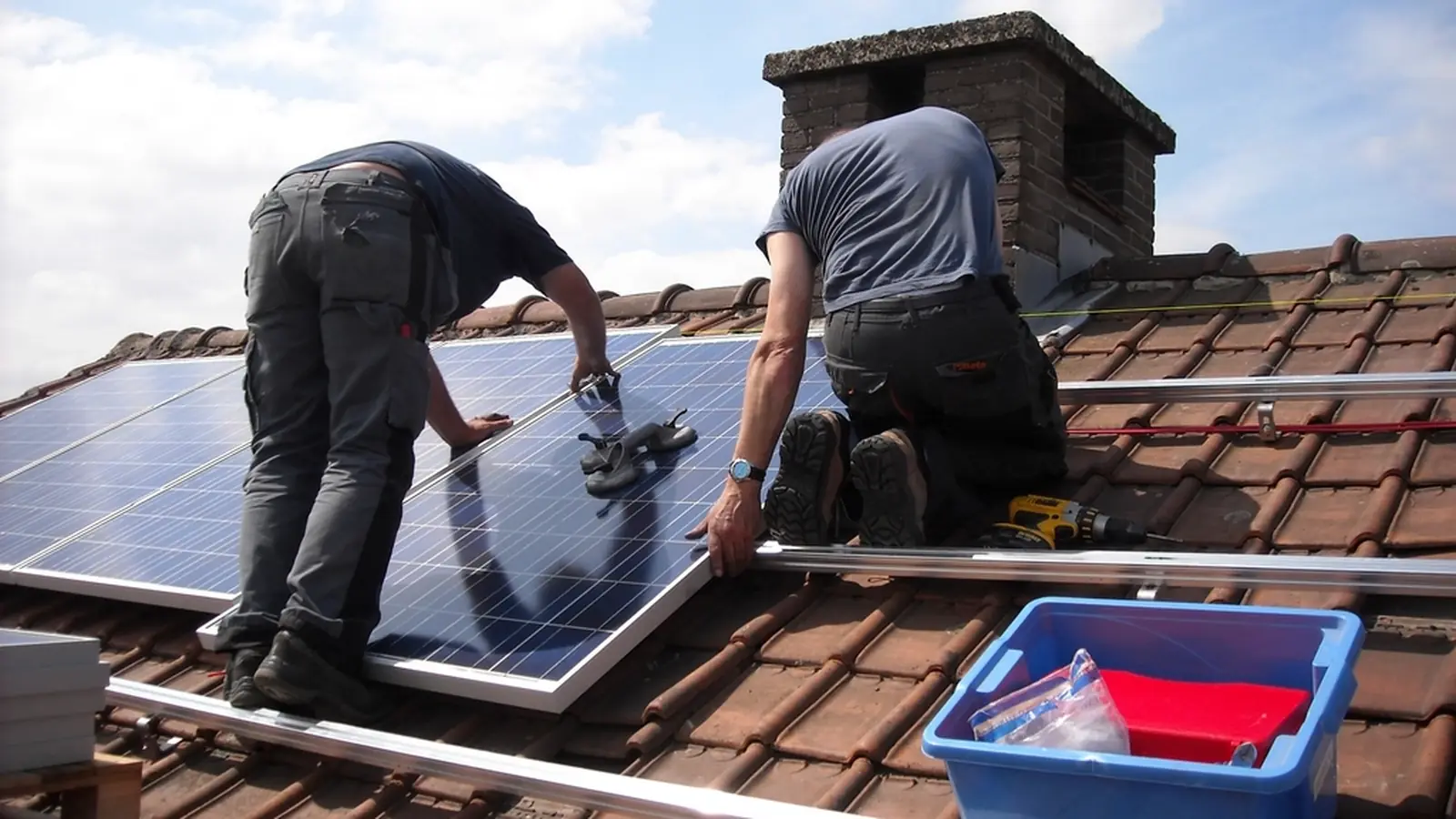 Two installers positioning a solar panel on a tiled roof